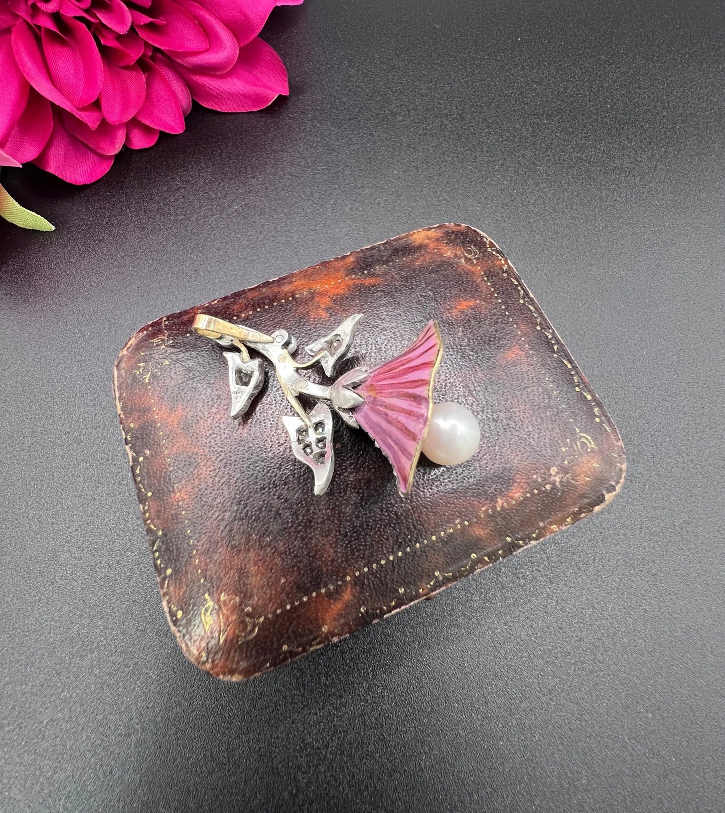 A pink enamel, diamond and pearl flower pendant in gold and silver, on an antique box