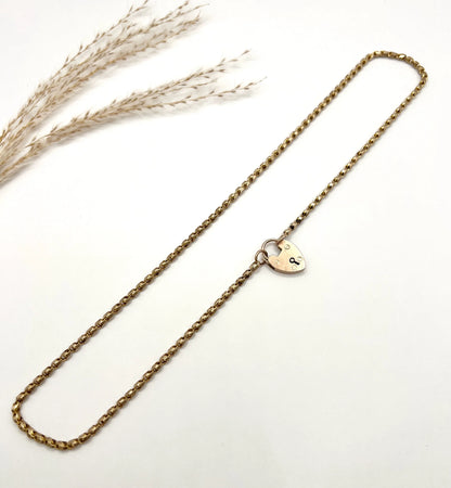 A gold chain necklace with gold heart padlock, laid flat on a white background