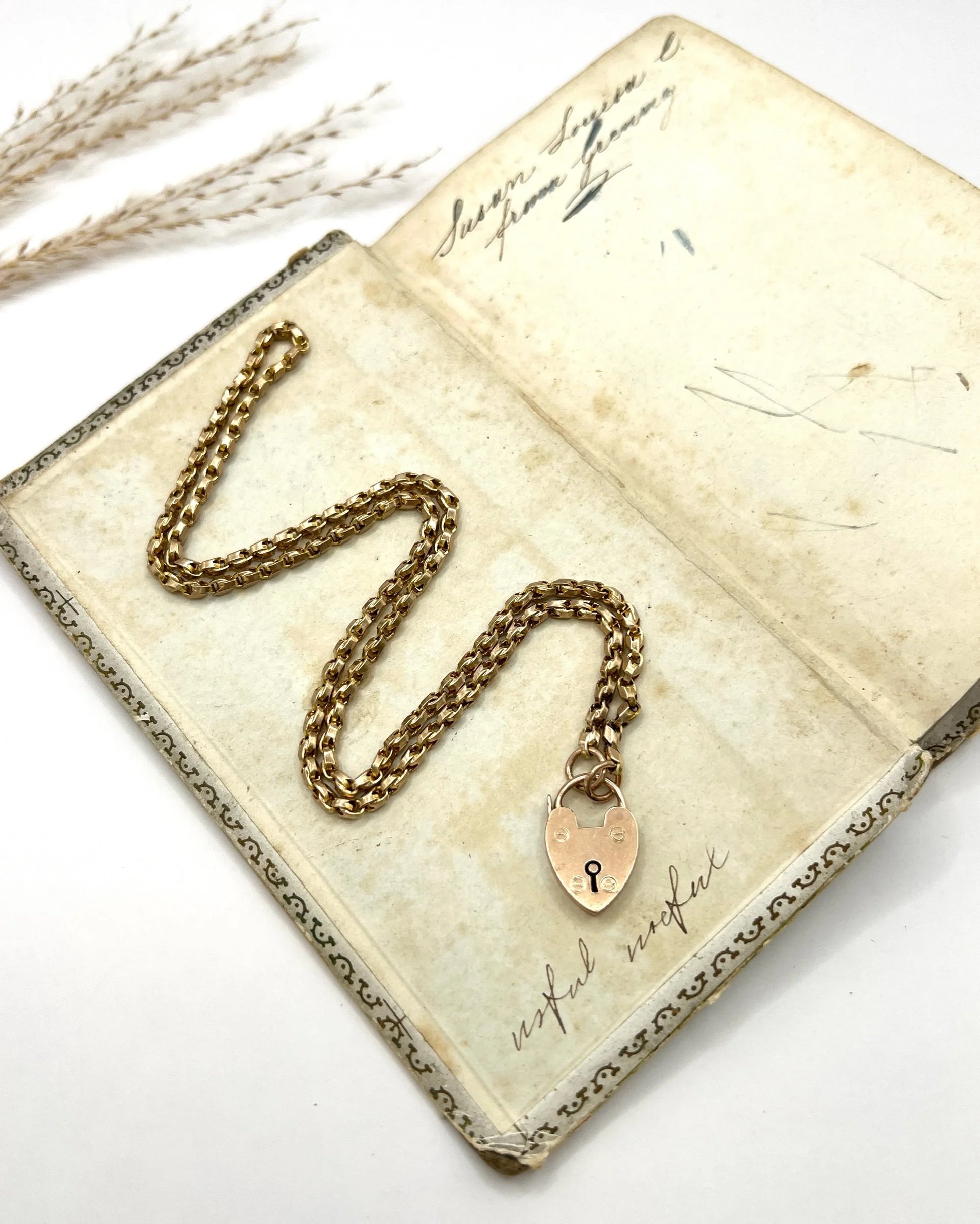 A gold chain necklace withgold heart padlock, on an antique book
