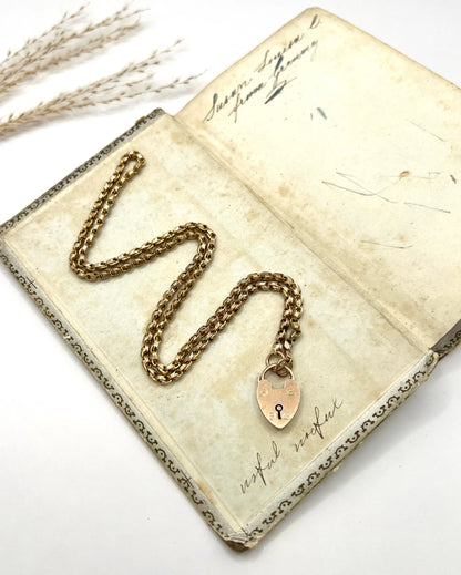 A gold chain necklace withgold heart padlock, on an antique book