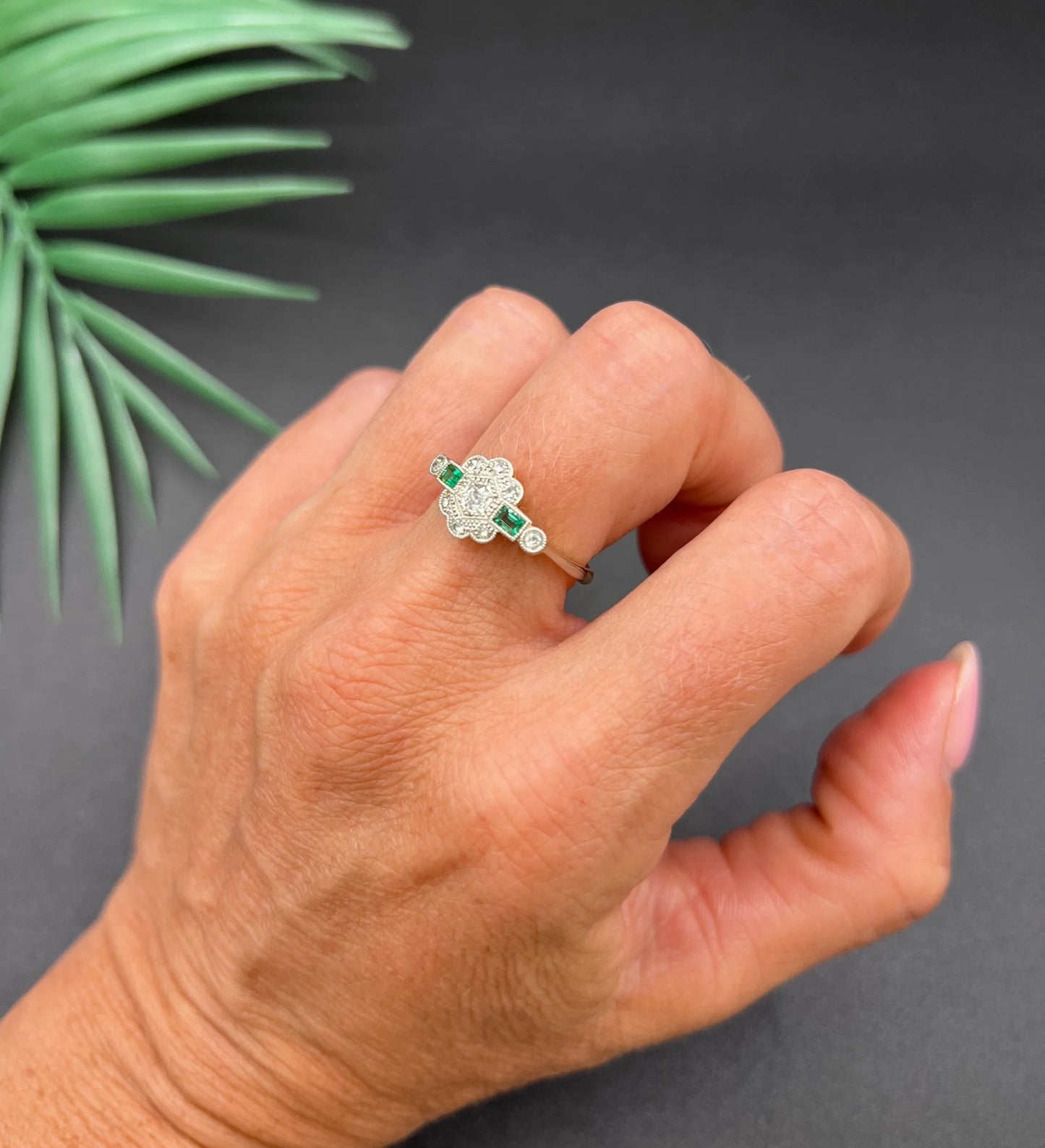 An emerald and diamond floral cluster ring in yellow gold and platinum, modelled on a hand