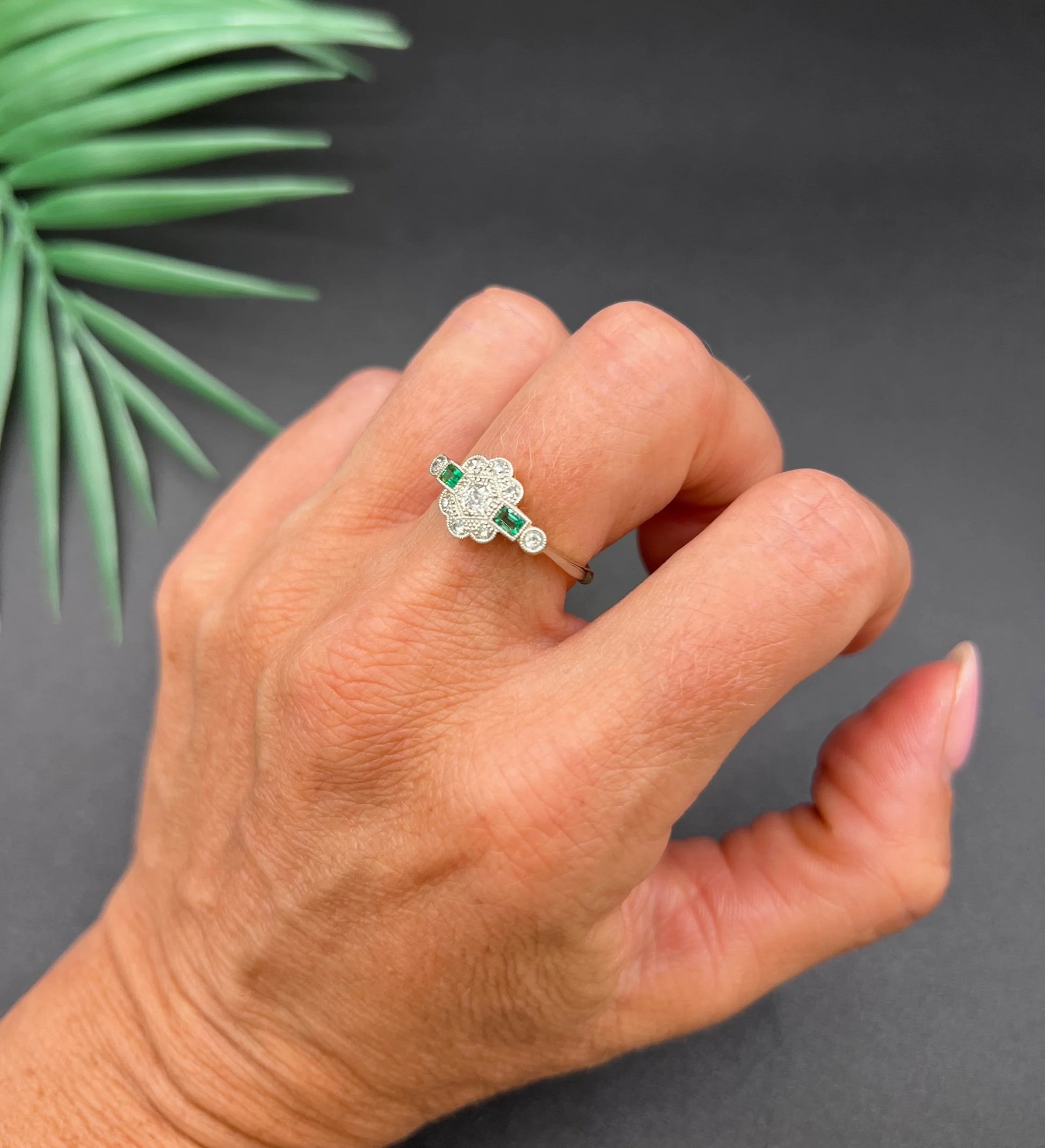 An emerald and diamond floral cluster ring in yellow gold and platinum, modelled on a hand
