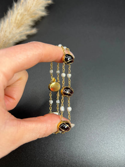 A yellow gold bracelet with oval cabochon garnets and white pearls, held in a hand
