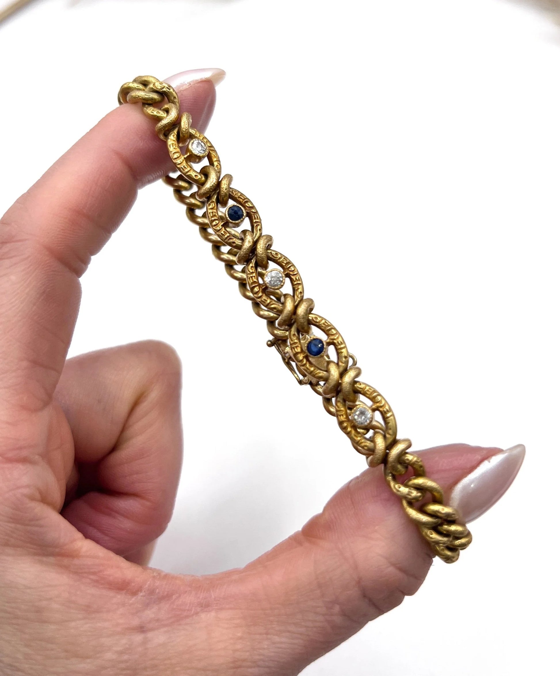A sapphire and diamond fancy curb link bracelet in yellow gold, held in a hand