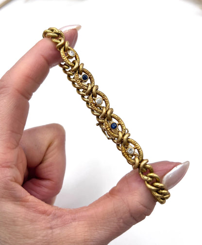 A sapphire and diamond fancy curb link bracelet in yellow gold, held in a hand