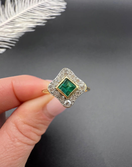 An emerald and diamond cluster ring in yellow gold and platinum, held in a hand
