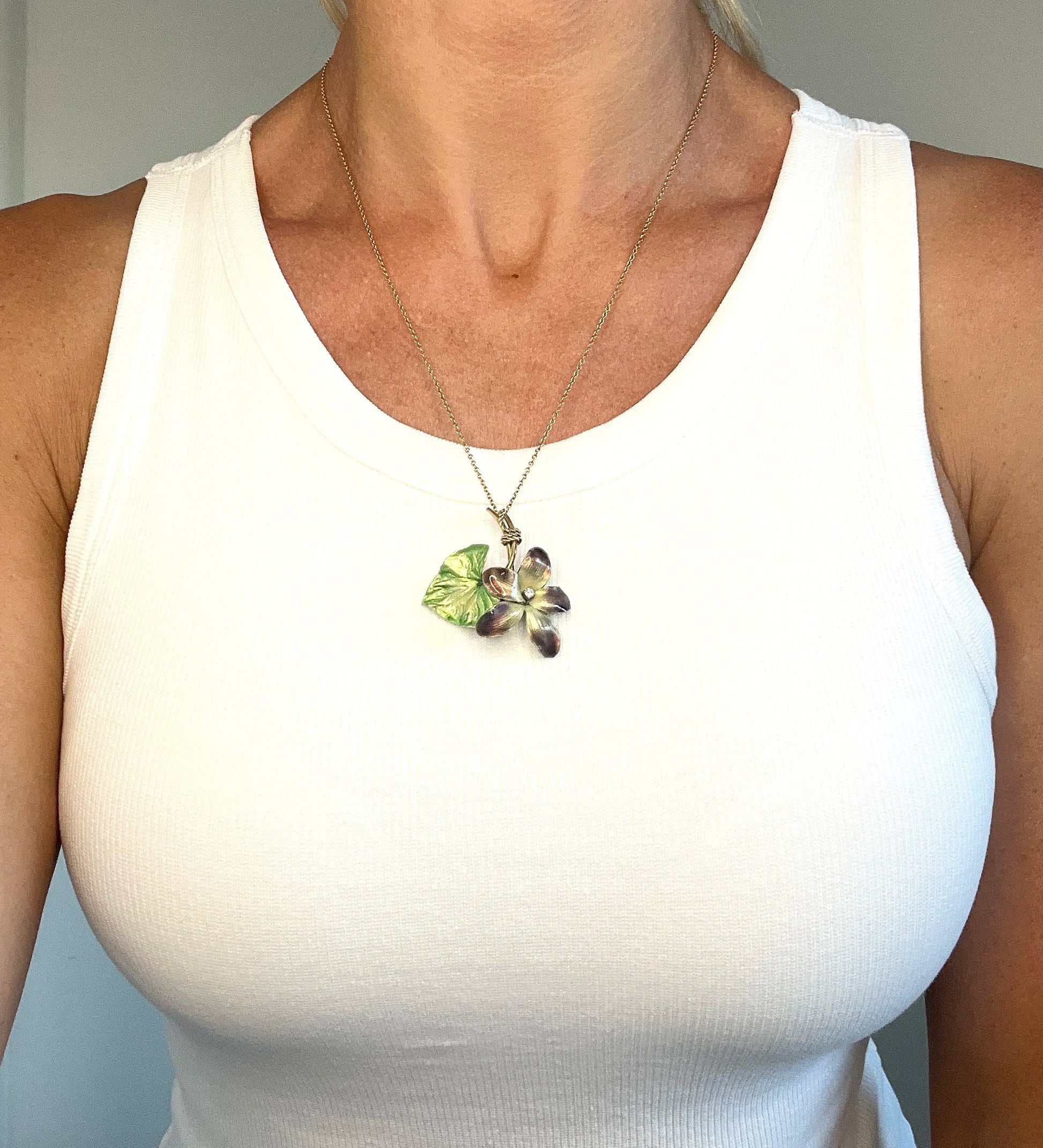 Gold and enamel diamond flower pendant modelled by a lady wearing a white top
