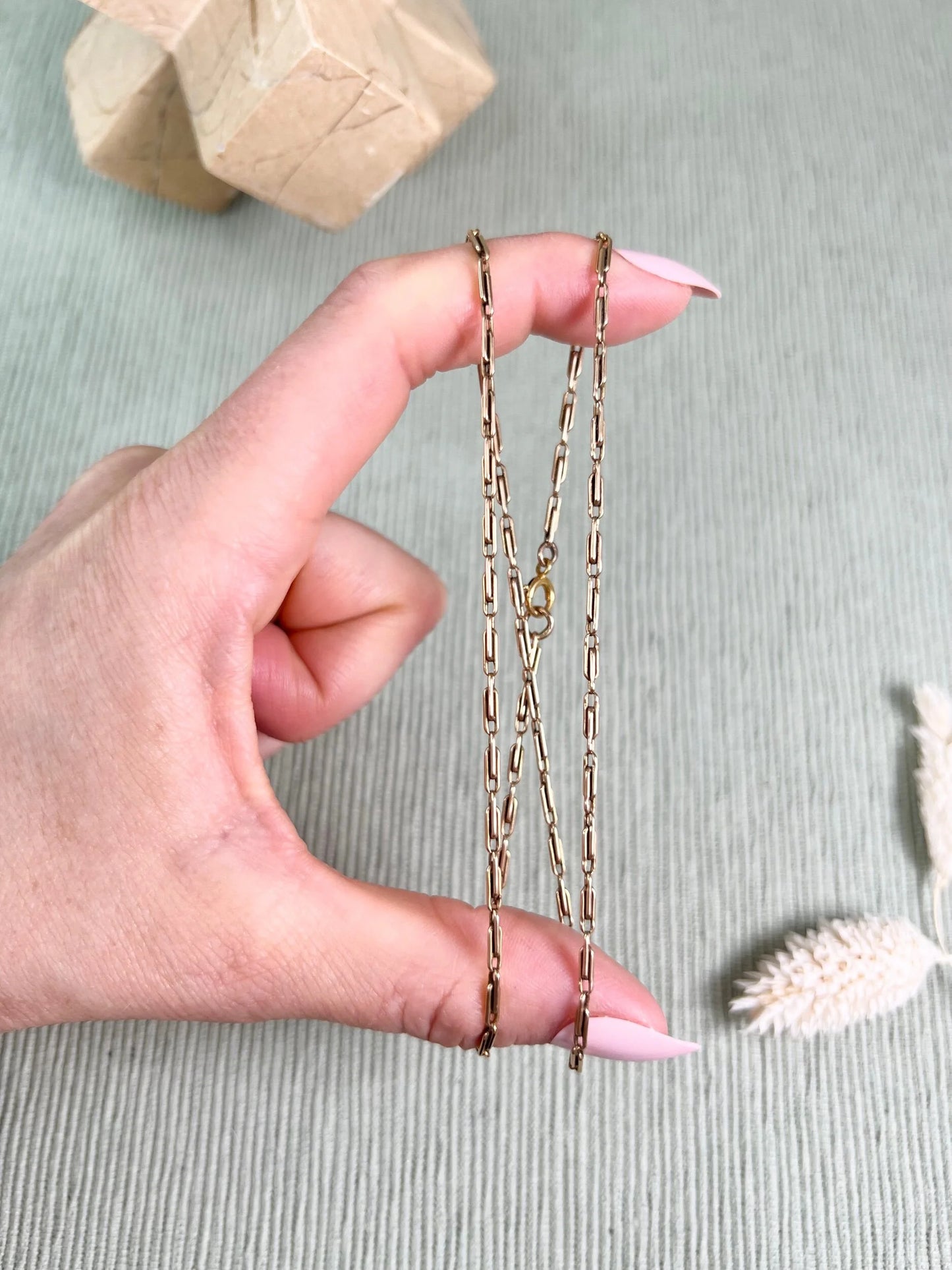 A gold paperclip link chain necklace held in a hand