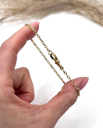 A yellow gold link bracelet with a lobster claw clasp, held in a hand