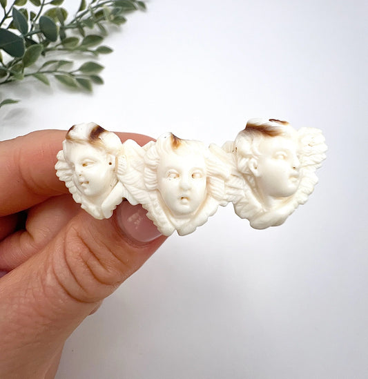 A triple cherub carved antique brooch, held in a hand
