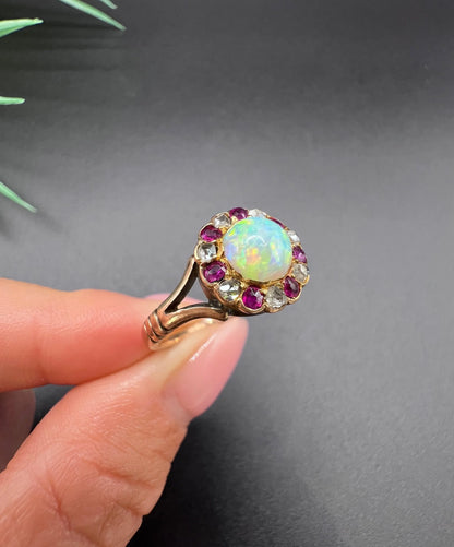 A daisy style cluster ring in rose gold with opal, ruby and diamond, held in a hand