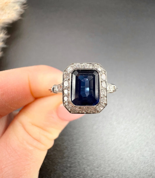An octagonal cluster ring with sapphire and diamonds in white gold, held in a hand