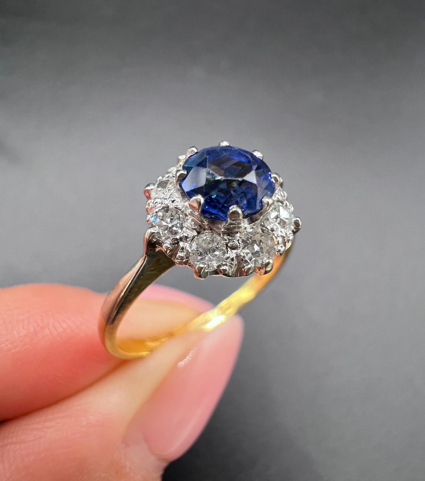 A circular cluster ring with sapphire and diamonds in yellow gold and platinum, held in a hand