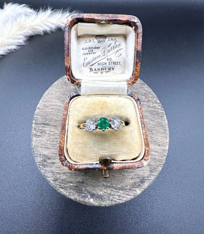 A three stone emerald and diamond ring in yellow gold and platinum, in an antique ring box
