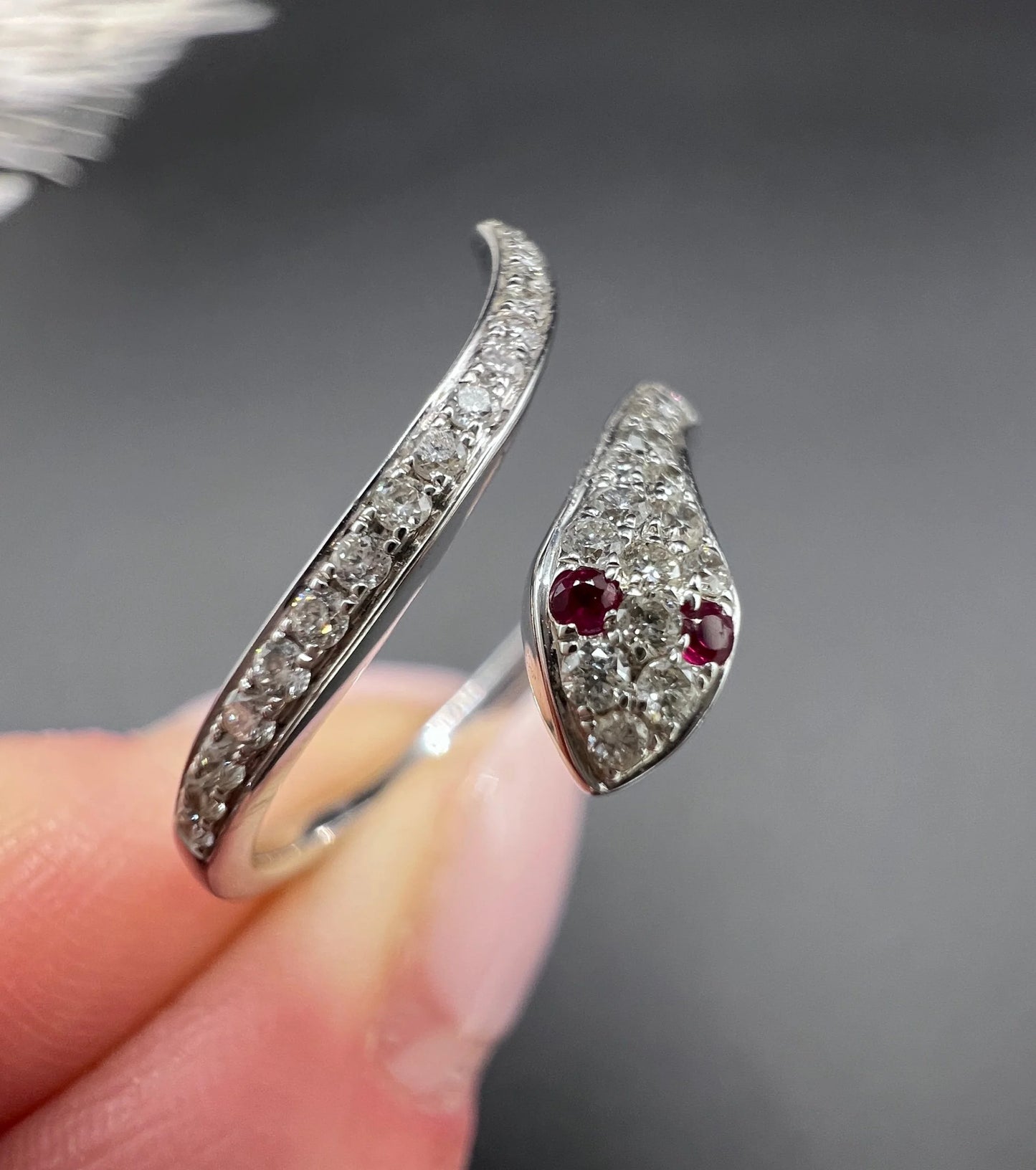 A white gold snake ring set with diamonds and with ruby eyes, held in a hand