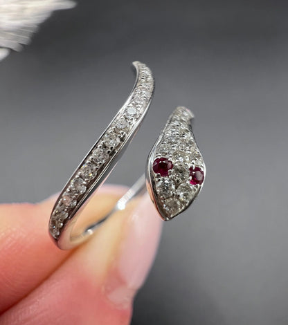 A white gold snake ring set with diamonds and with ruby eyes, held in a hand