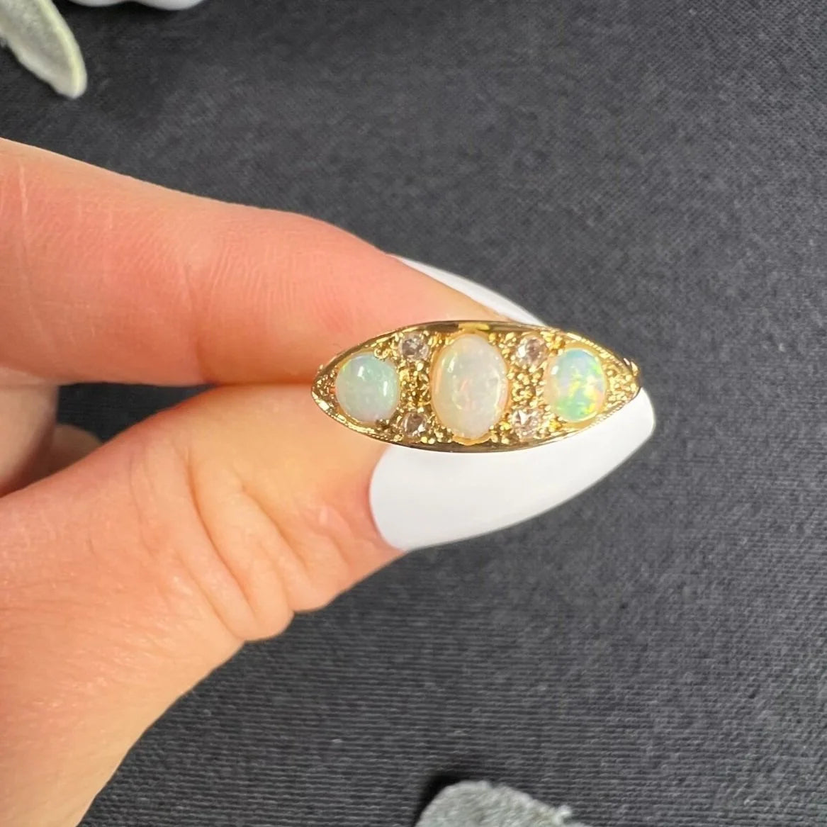 A boat-shaped gold ring with opals and diamonds, held in a hand