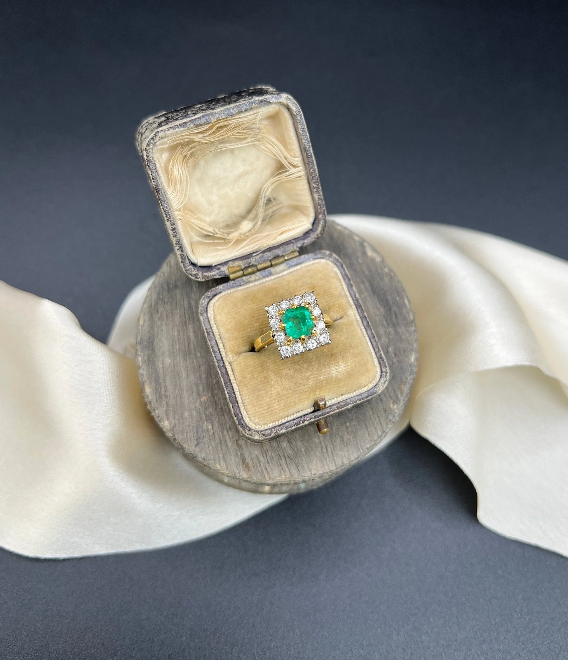 A square shaped emerald and diamond cluster ring in yellow and white gold, in a ring box