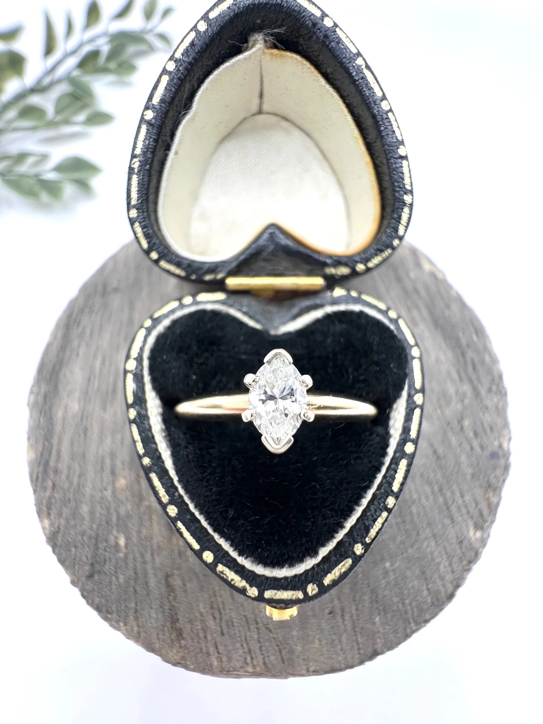 A marquise diamond solitaire ring in yellow and white gold, in a heart-shaped ring box
