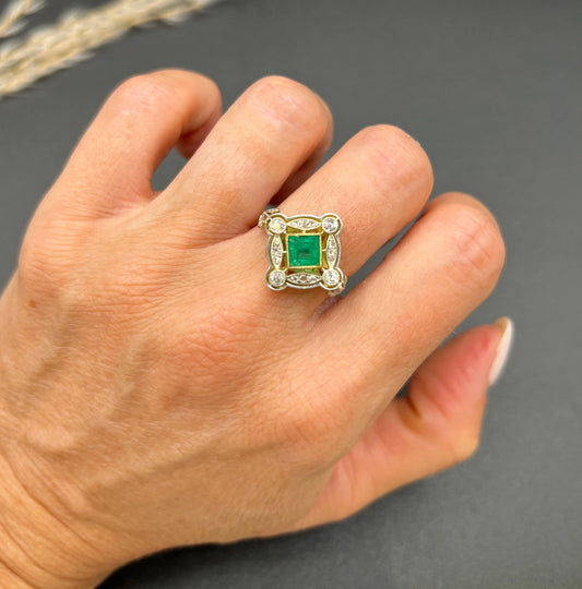 A gold and platinum ring with a centre emerald and diamond surround, modelled on a hand