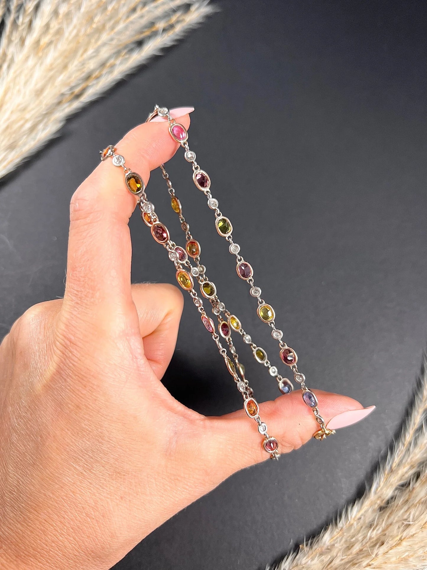 A coloured sapphire and diamond set necklace in platinum and gold, held in a hand