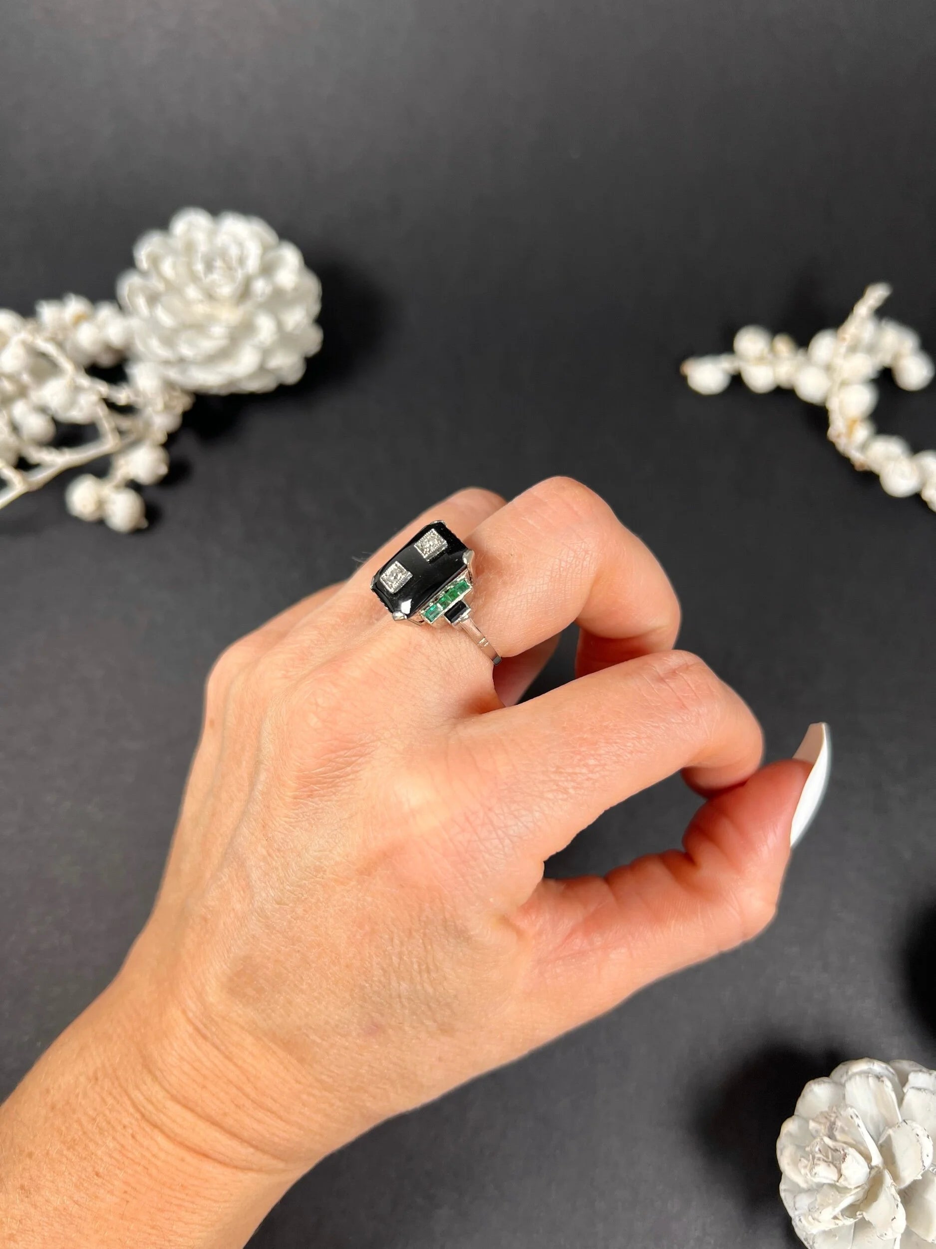 A geometric black onyx ring with diamonds and emeralds in white gold, modelled on a hand