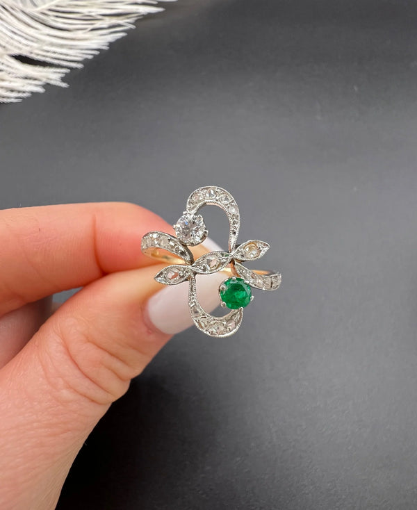 An emerald and diamond fancy openwork ring in yellow gold and platinum, held in a hand
