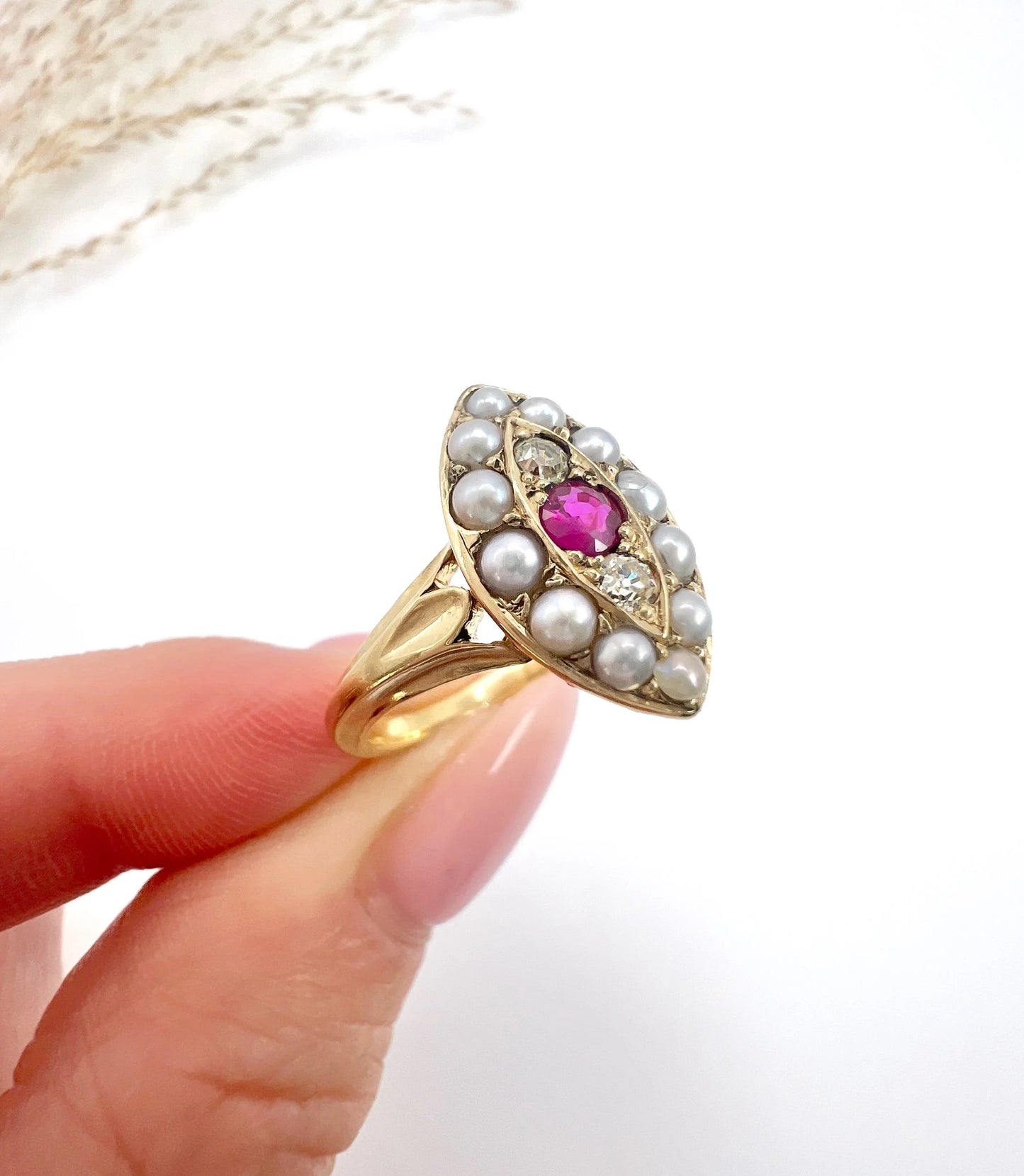 A navette shaped pearl, diamond and ruby cluster ring in yellow gold, held in a hand