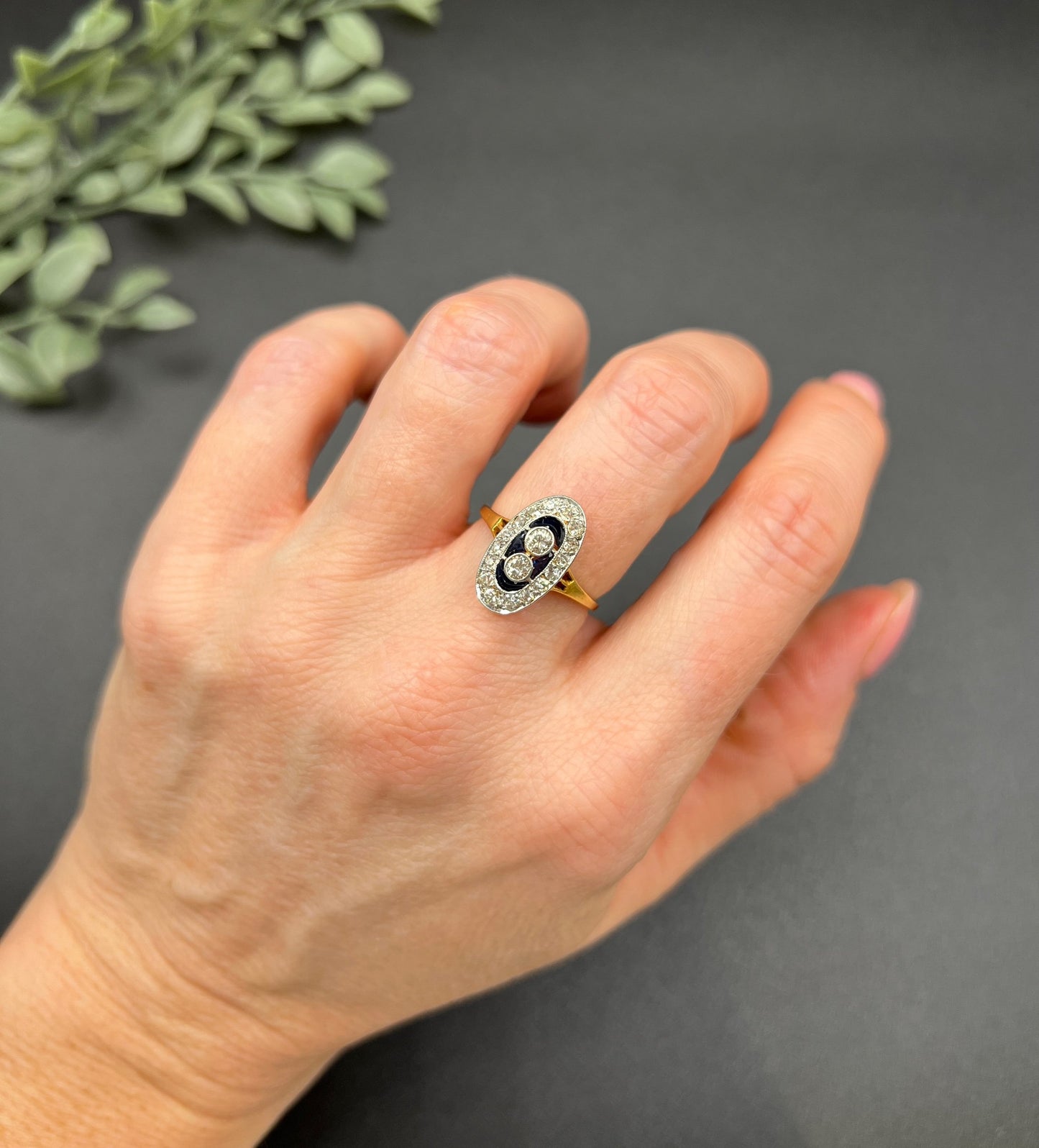 An oval cluster ring with diamonds and sapphires in platinum and yellow gold, modelled on a hand