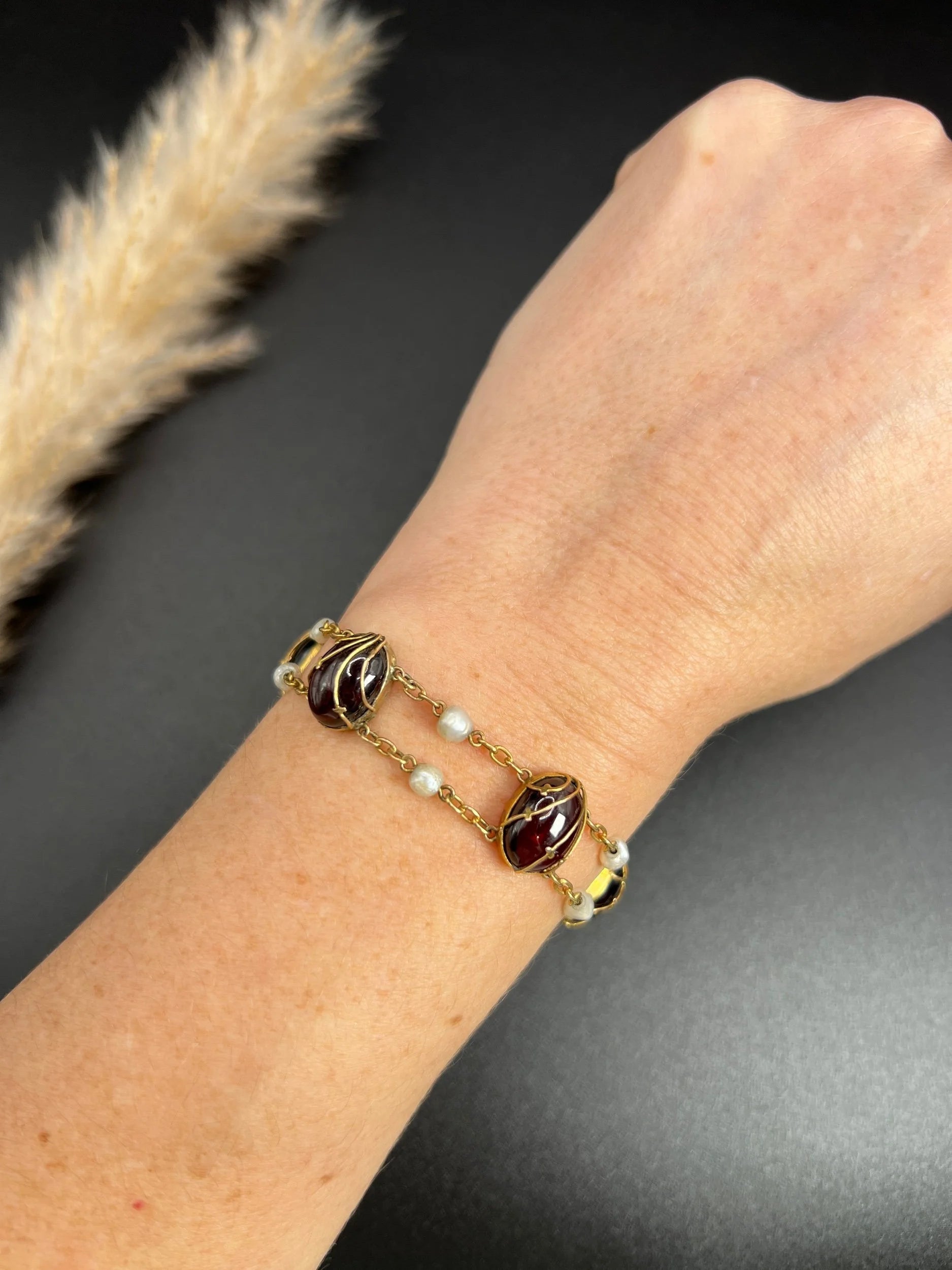 A yellow gold bracelet with oval cabochon garnets and white pearls, modelled on a wrist