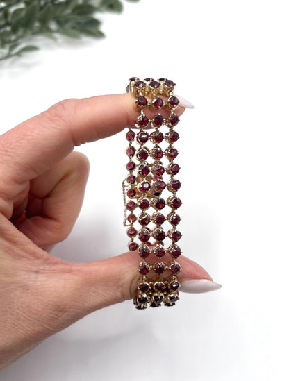 A triple row garnet bracelet in rose gold, held in a hand