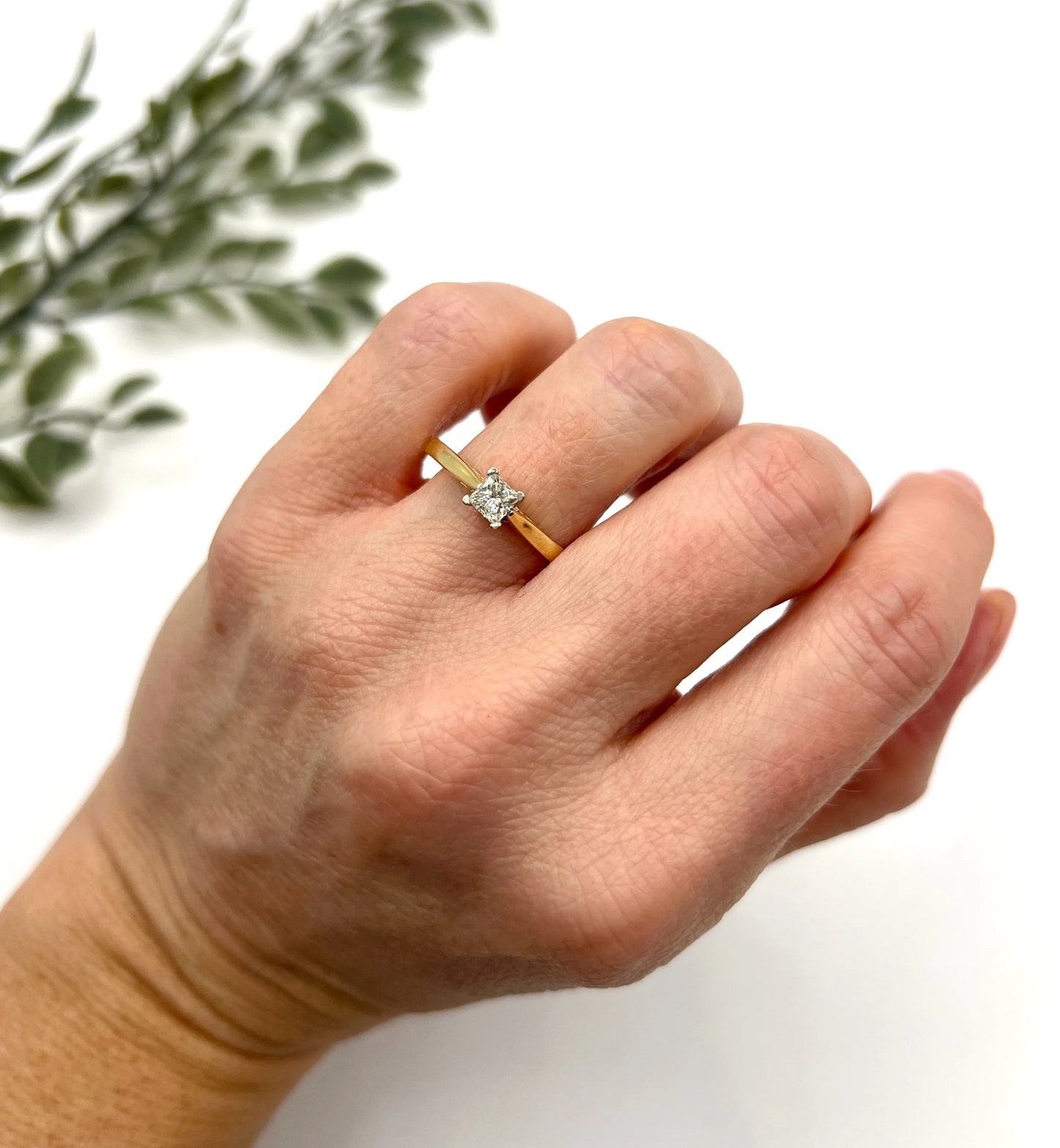 A solitaire princess cut diamond ring in yellow and white gold, modelled on a hand