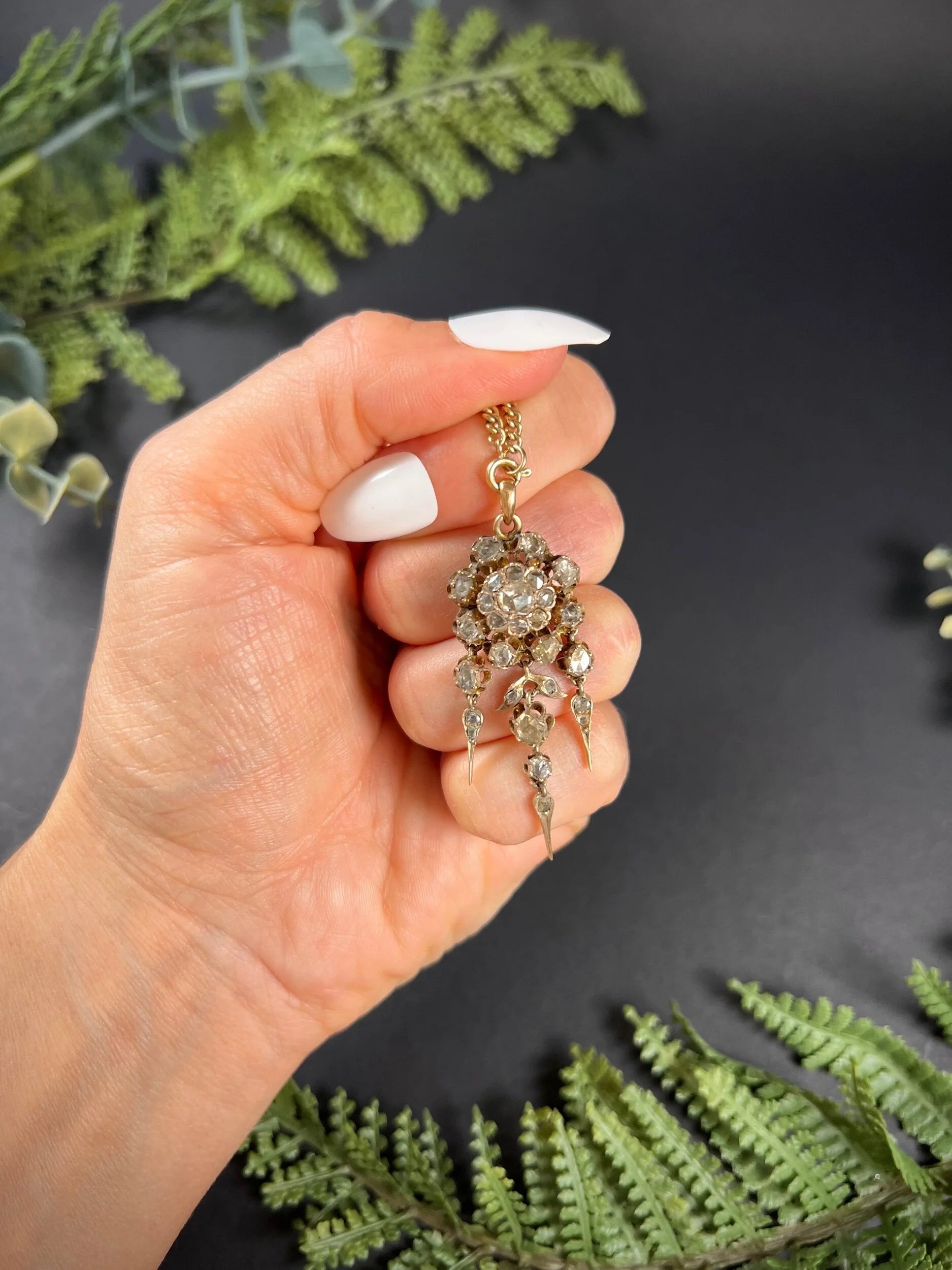 A yellow gold pendant with old cut diamonds, with a gold chain, held by a hand