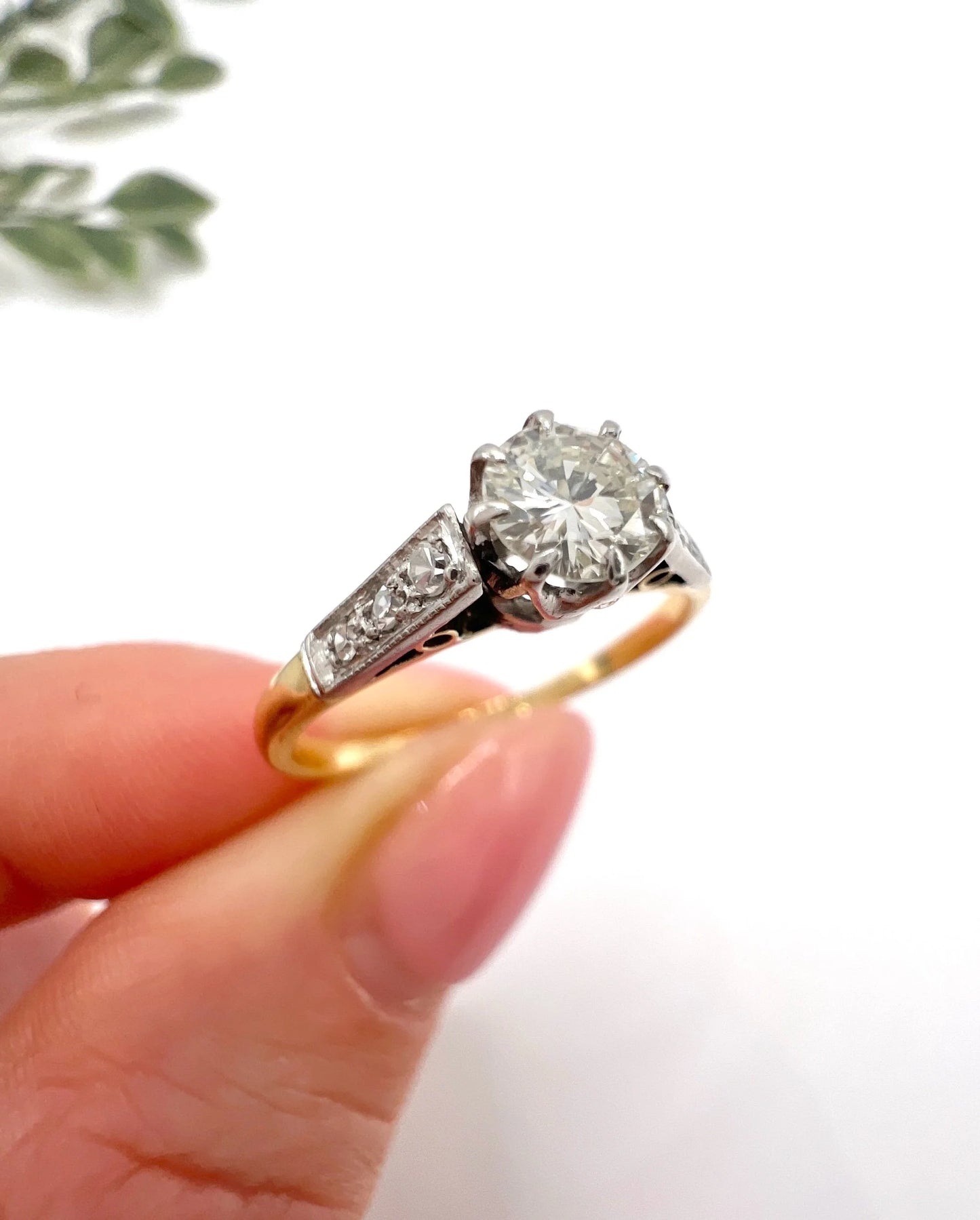 A diamond engagement style ring in yellow gold and platinum, held in a hand