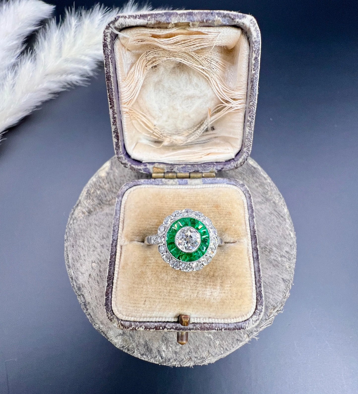 An emerald and diamond target cluster ring in platinum, in a ring box