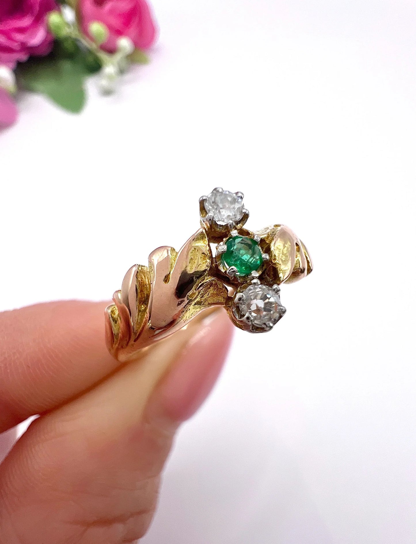 A three stone emerald and diamond ring in yellow and white gold, held in a hand