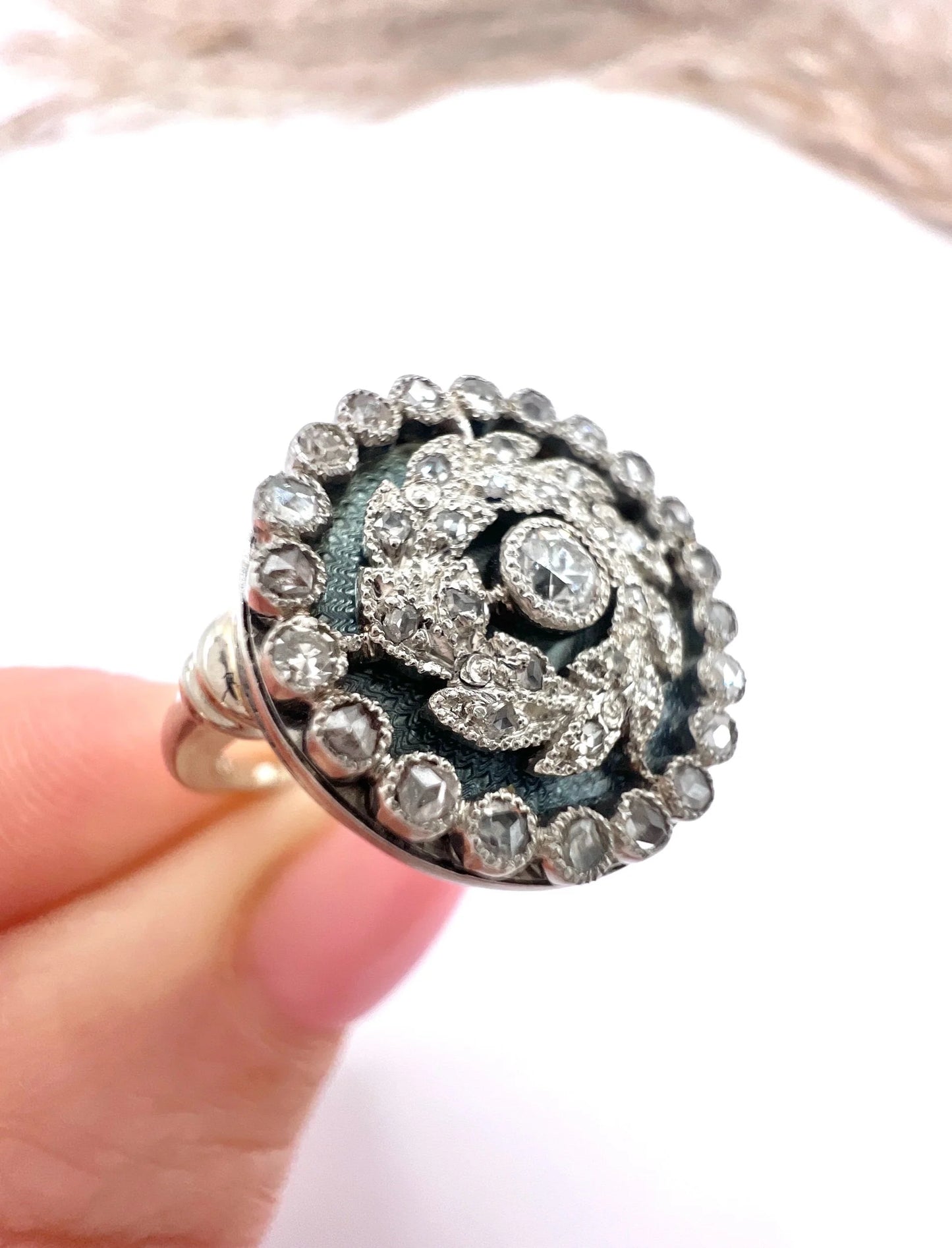 A diamond and dark blue enamel fancy cluster ring in white gold, held in a hand
