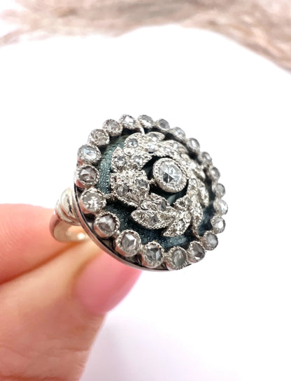 A diamond and dark blue enamel fancy cluster ring in white gold, held in a hand