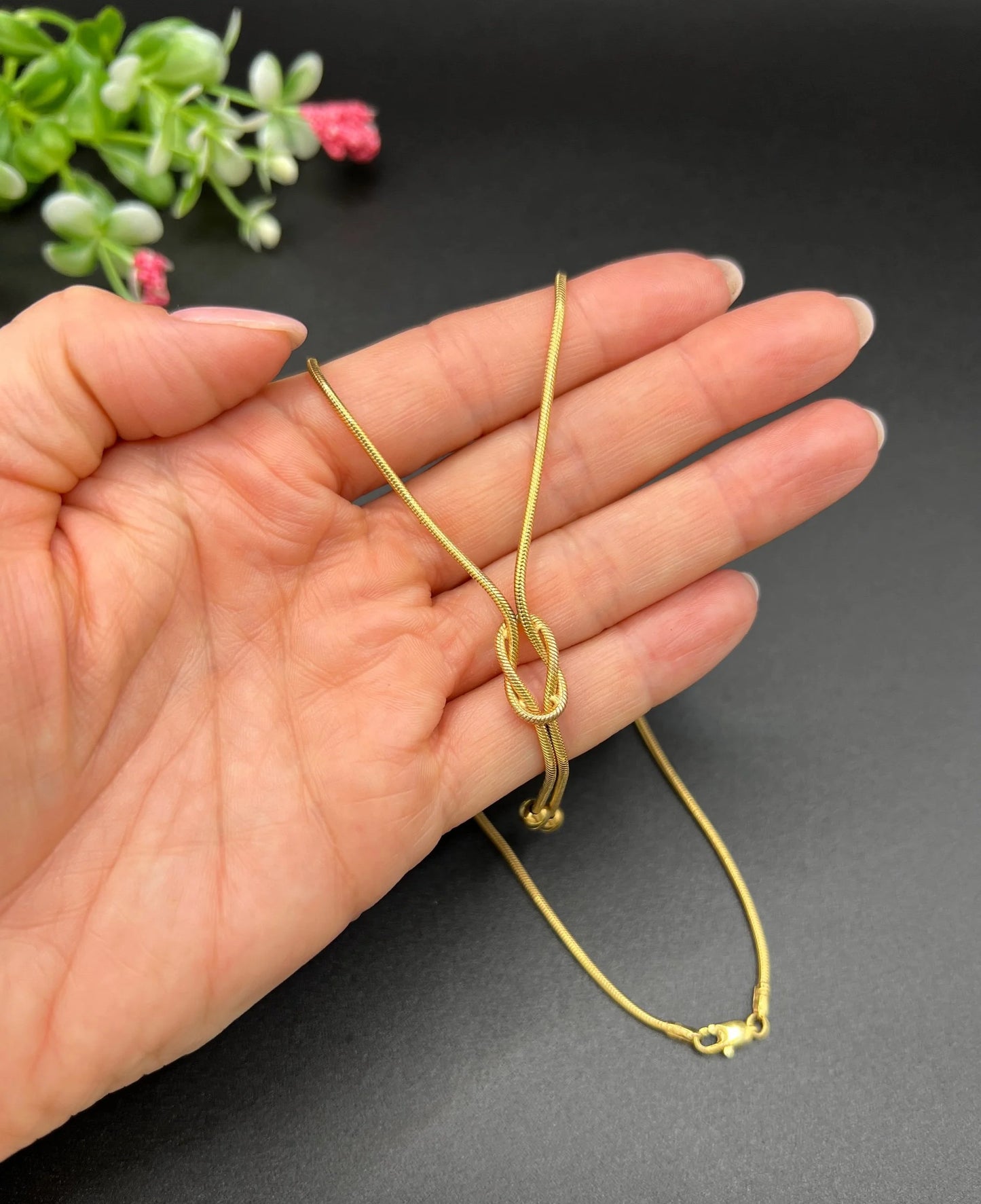 A yellow gold snake link chain necklace with a knot and tassel drop, held in a hand