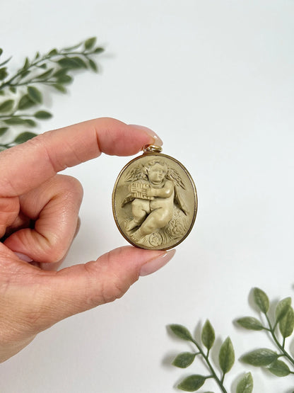 An oval cherub lava cameo pendant in yellow gold, held in a hand