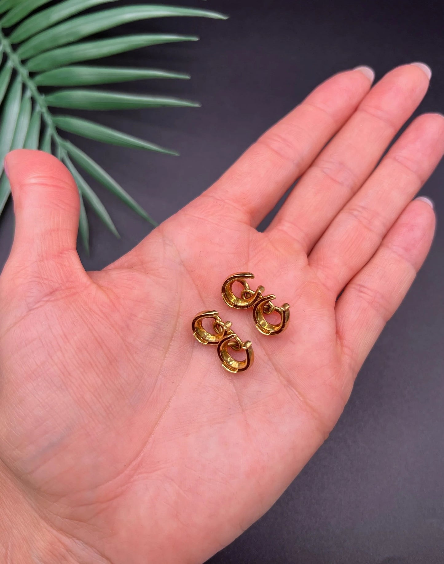 A pair of double-sided horseshoe cufflinks in yellow gold, held in a hand