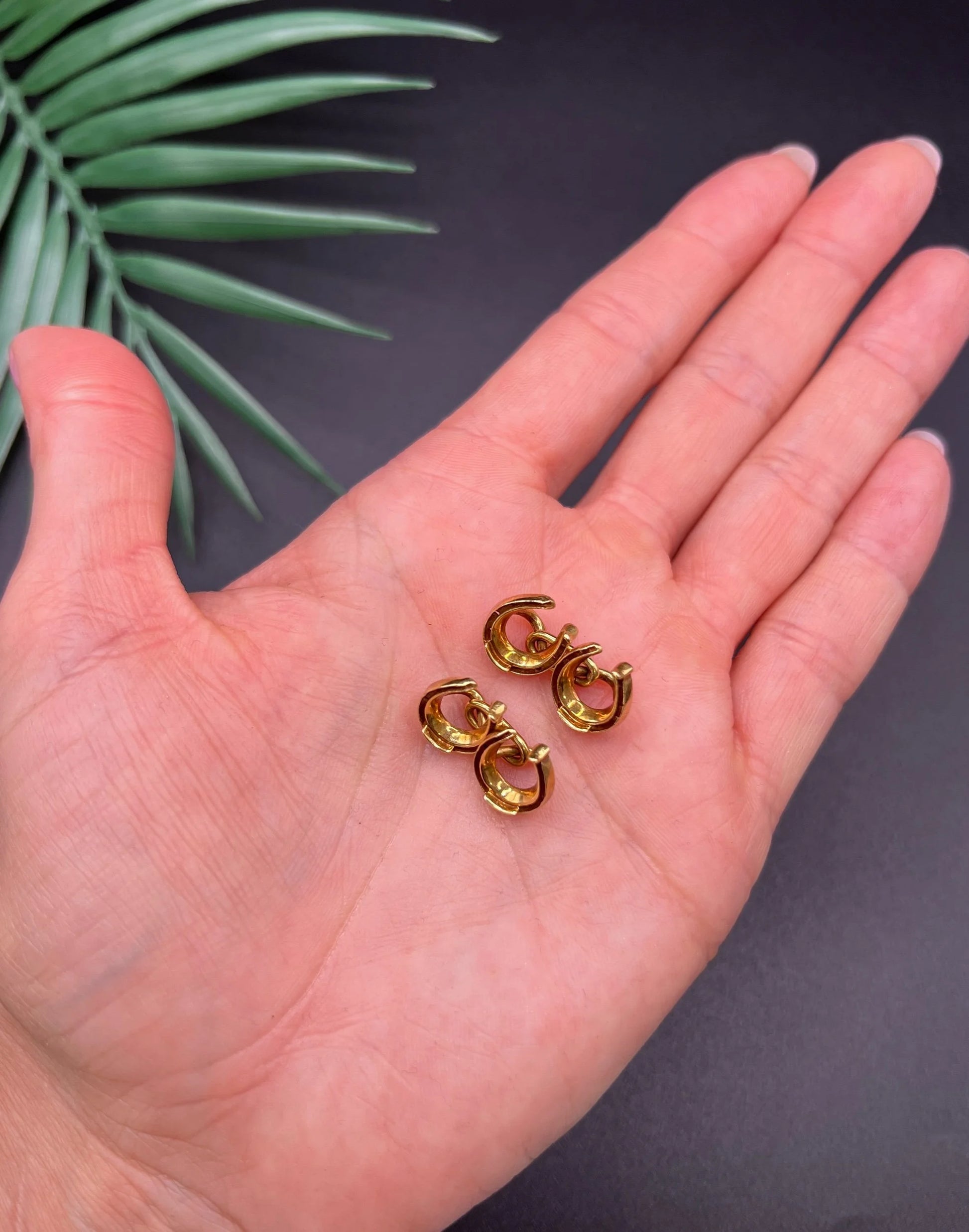 A pair of double-sided horseshoe cufflinks in yellow gold, held in a hand