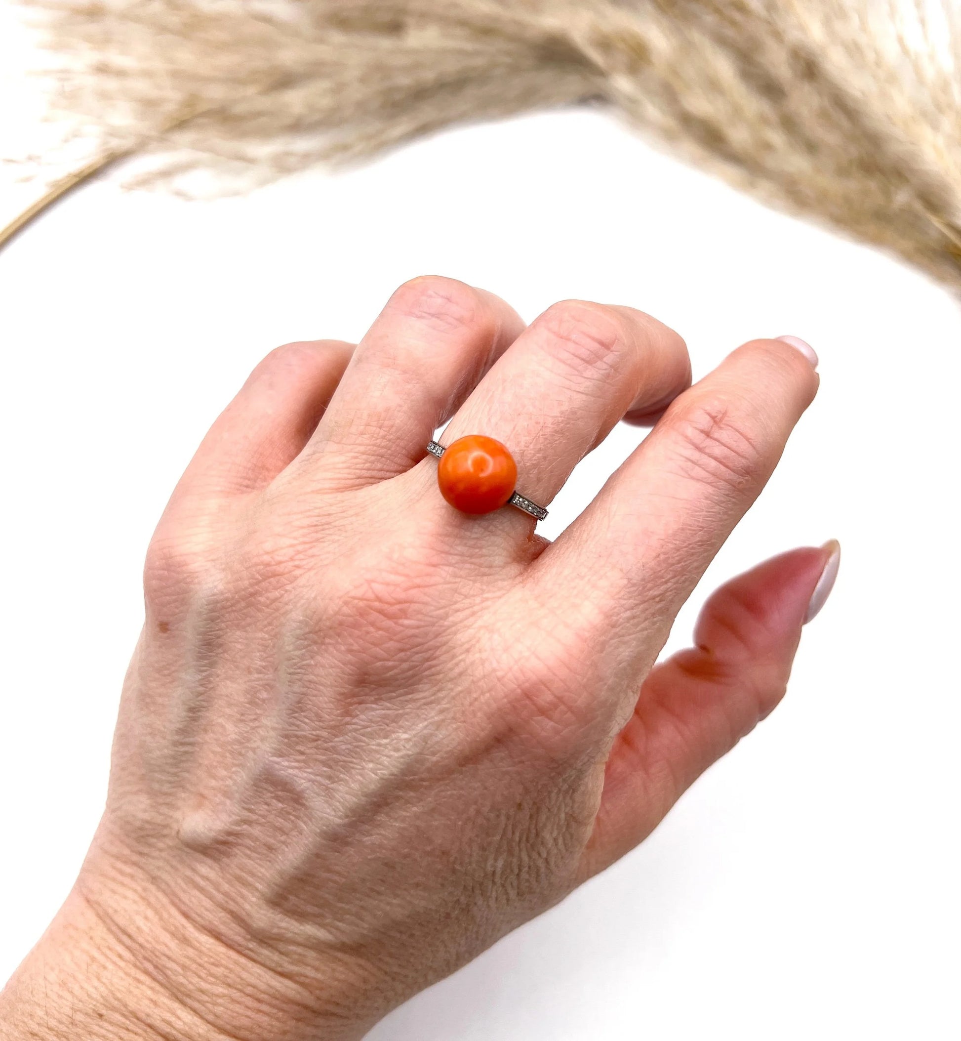A round orange coral and diamond dress ring in platinum, modelled on a hand