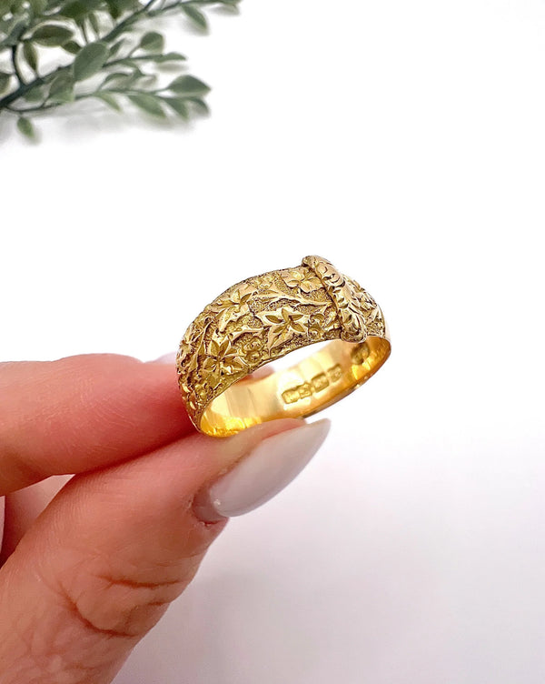 A yellow gold ornate engraved buckle band ring, held in a hand