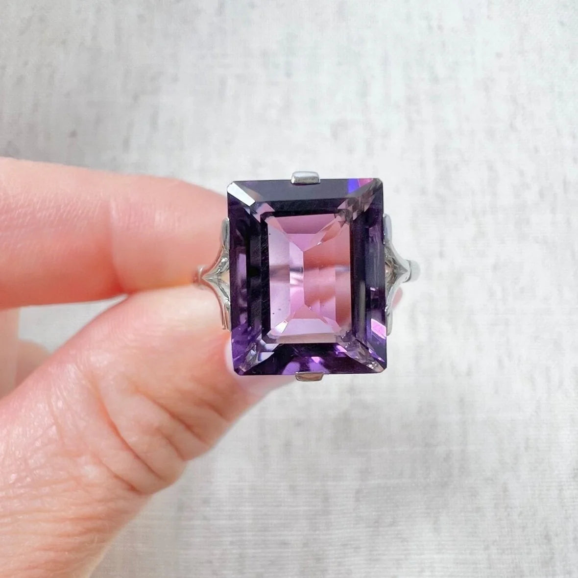 A solitaire amethyst cocktail ring in platinum, held in a hand