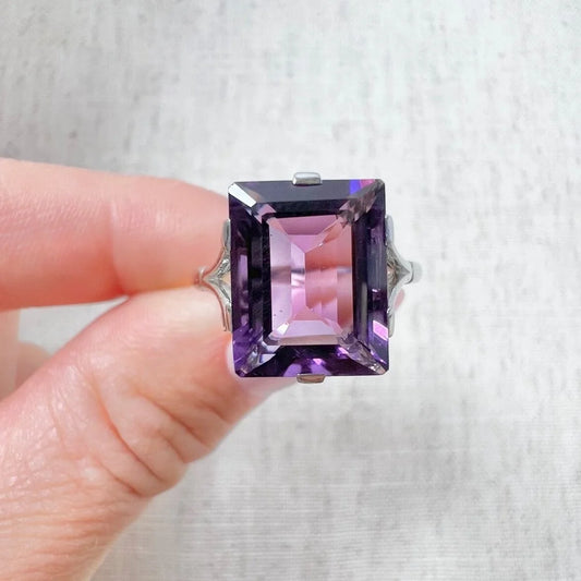 A solitaire amethyst cocktail ring in platinum, held in a hand