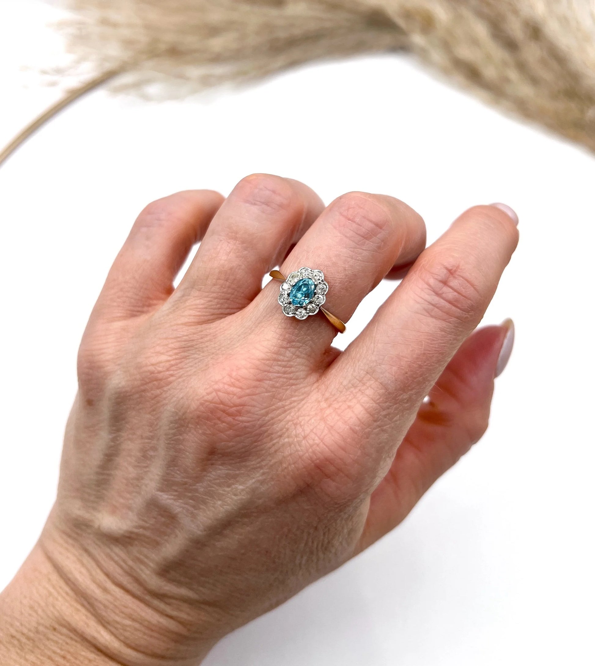 An oval cluster ring with a blue zircon centre surrounded by round diamonds, in yellow gold and platinum, modelled on a hand