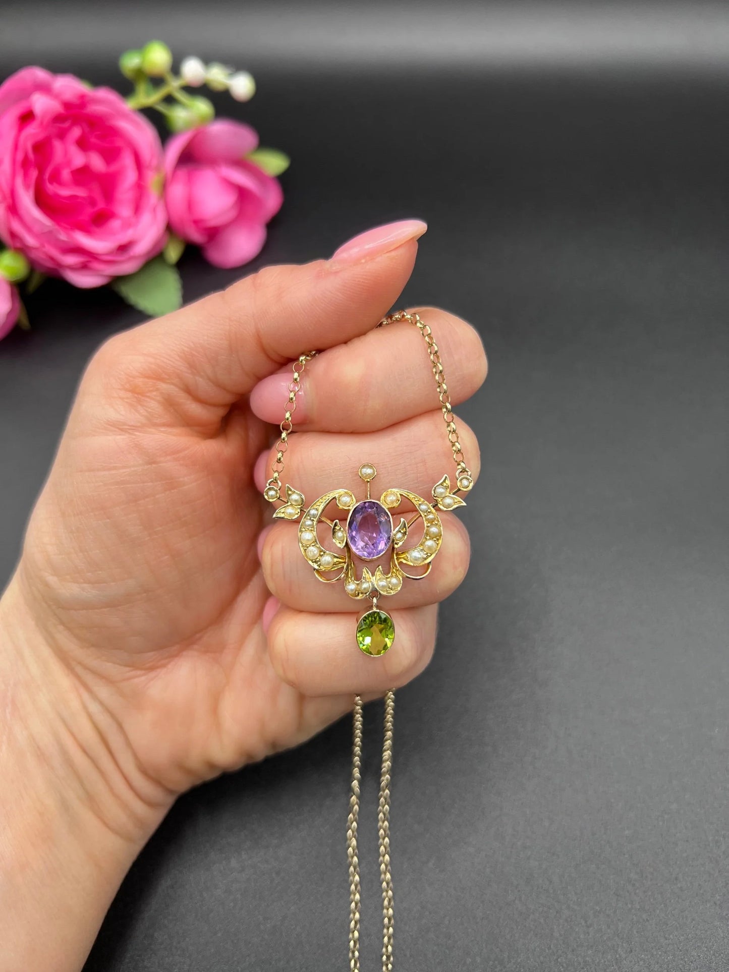 A yellow gold peridot, amethyst and seed pearl pendant necklace, held in a hand