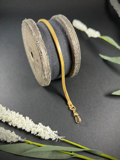 A yellow gold snake link bracelet, laid on a wooden spool