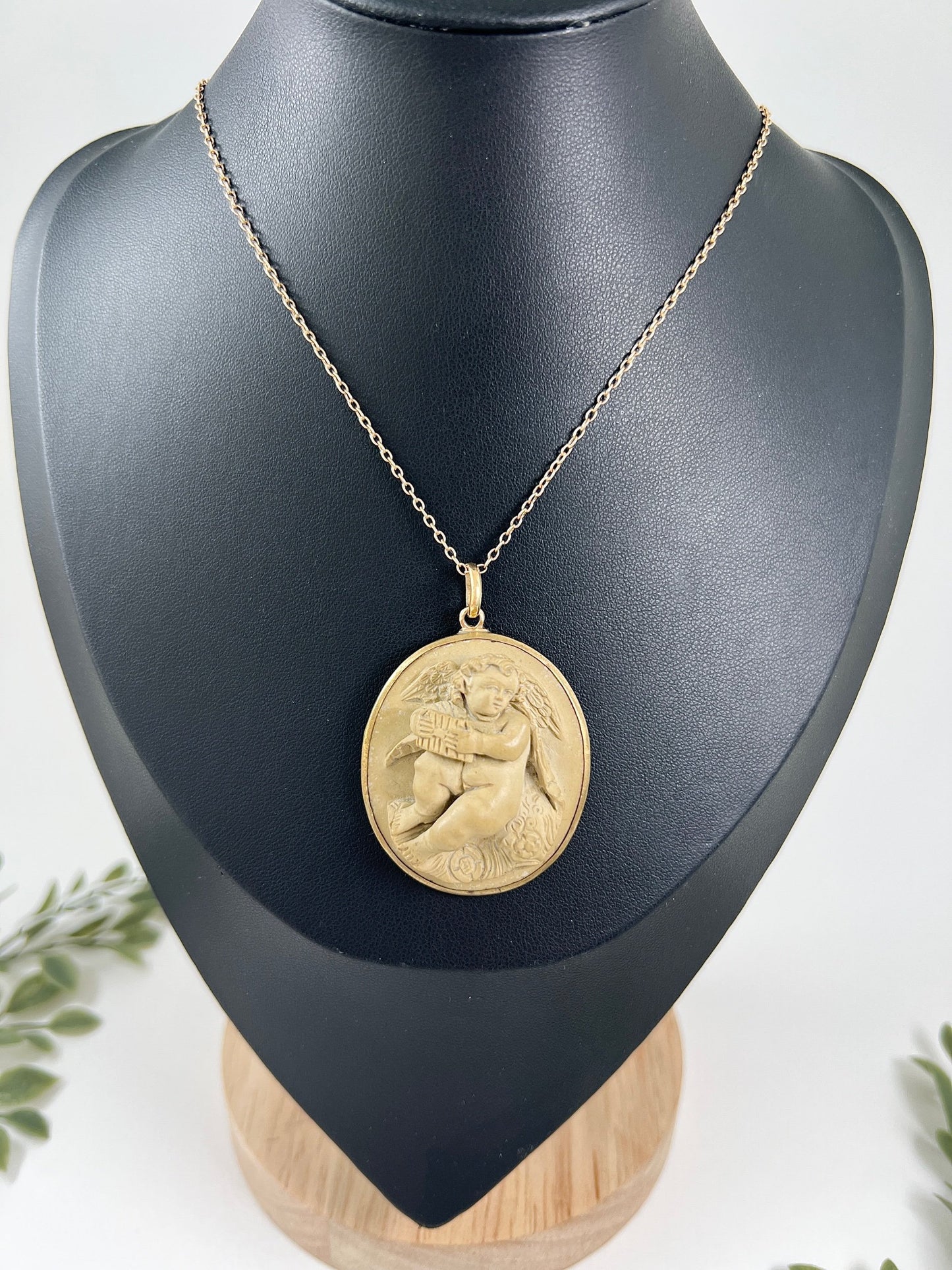 An oval cherub lava cameo pendant in yellow gold, with a chain, on a black bust